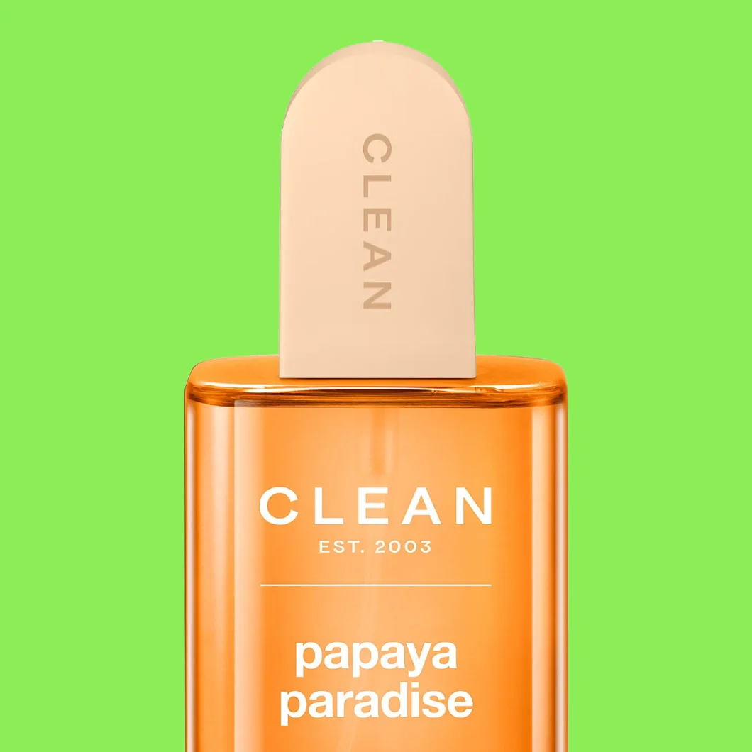 Parfymflaska i orange med texten “CLEAN EST. 2003 papaya paradise” och kork märkt “CLEAN” mot grön bakgrund.