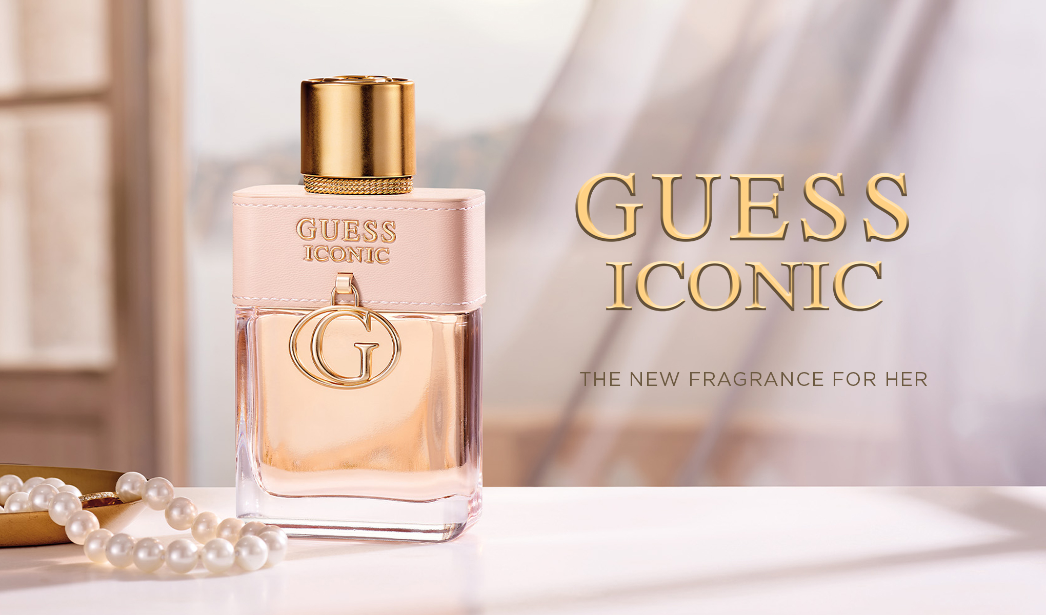 En elegant parfymeflaske med Guess Iconic-logoen står på et bord ved siden av en perlekjede. Bakgrunnen er lys og luftig, med gardiner som skaper en sofistikert atmosfære.
