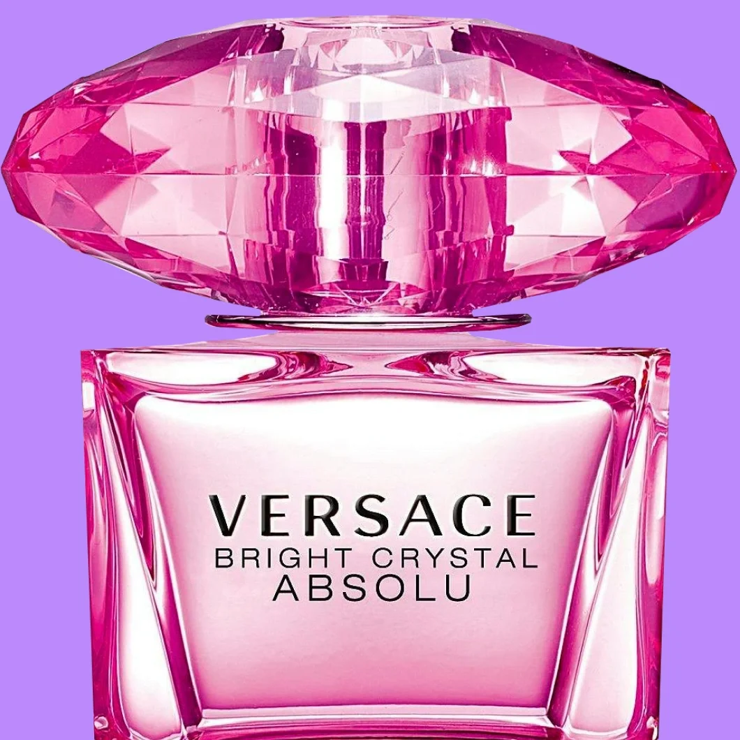 Lähikuva Versace Crystal Emerald Eau de Parfum -hajuvedestä smaragdinvihreässä lasipullossa, jossa on suuri fasetoitu vihreä korkki ja kullanvärinen teksti ”VERSACE CRYSTAL EMERALD EAU DE PARFUM”, violetilla taustalla.