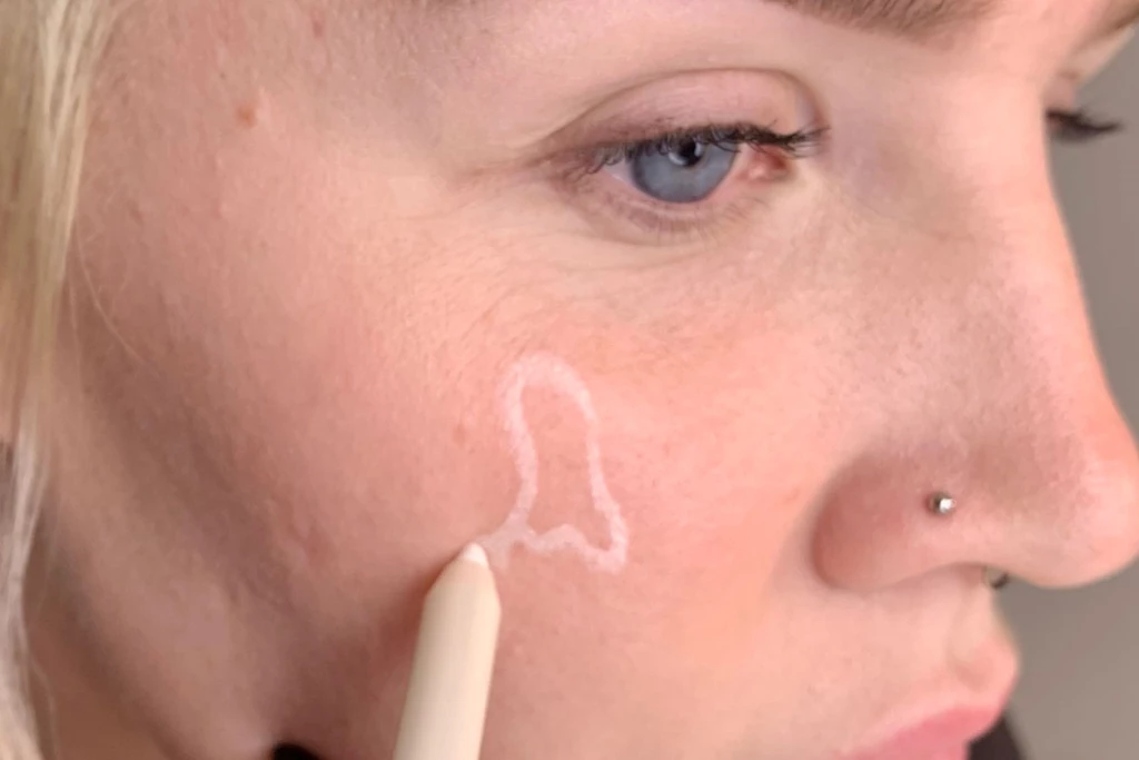 Person som tegner en hvit spøkelsesform på kinnet med en eyeliner-blyant.