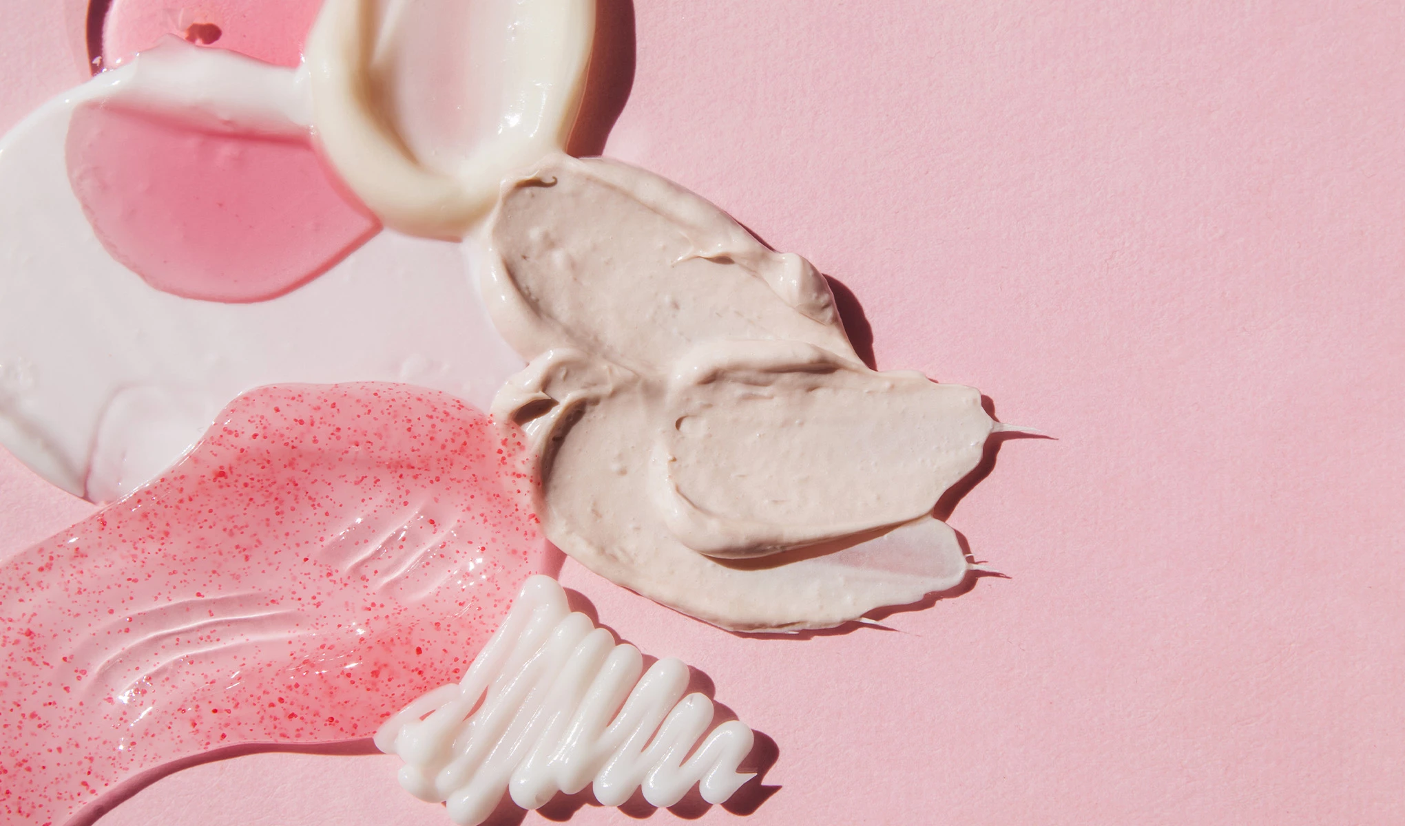 Olika typer av hudvårdsprodukter i kräm- och gelékonsistens utbredda på en rosa bakgrund.