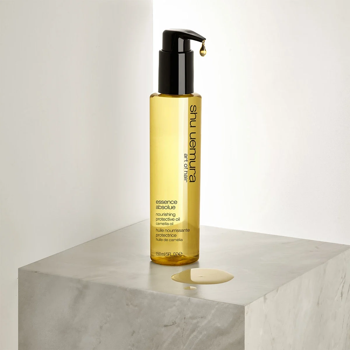 En flaske med Shu Uemura Essence Absolue nærende beskyttende olje, plassert på en hvit marmorkube. En dråpe olje har falt ved siden av flasken.
