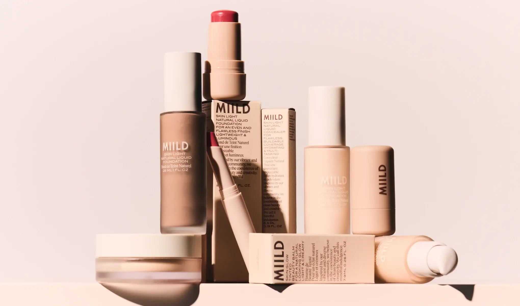 Sminkeprodukter fra MIILD mot en lys bakgrunn, blant annet foundation, blush og pudder.