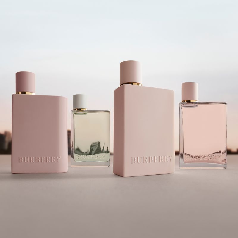 Fyra parfymer från Burberry i olika färger och former, placerade på en yta med en stadssilhuett i bakgrunden.