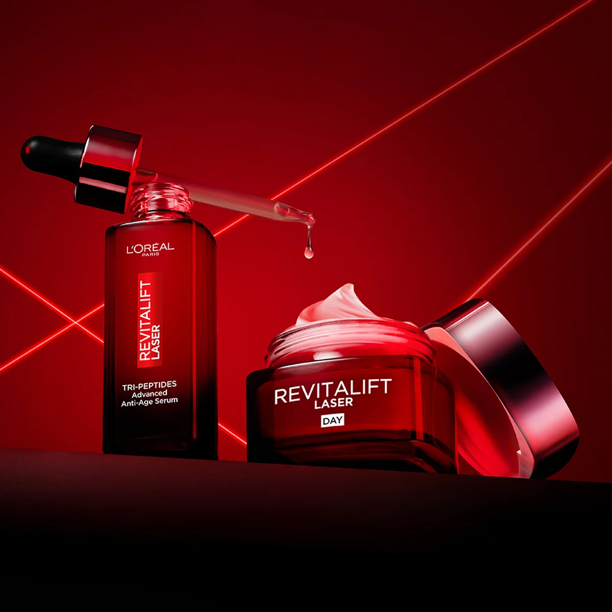 Två Revitalift Laser hudvårdsprodukter från L'Oréal mot en röd bakgrund. Ett serum med pipett och en öppen dagkräm med synlig kräm i locket.