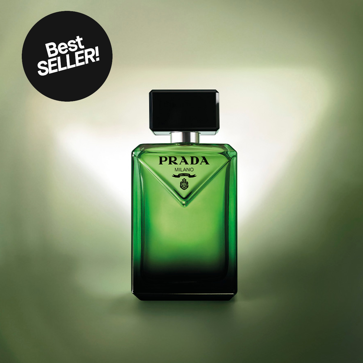 Grønn parfymeflaske fra Prada Milano med svart kork står mot myk grønn bakgrunn. Teksten “PRADA MILANO” vises på flasken og en svart sirkel med teksten “Best SELLER!” er plassert ved siden av.