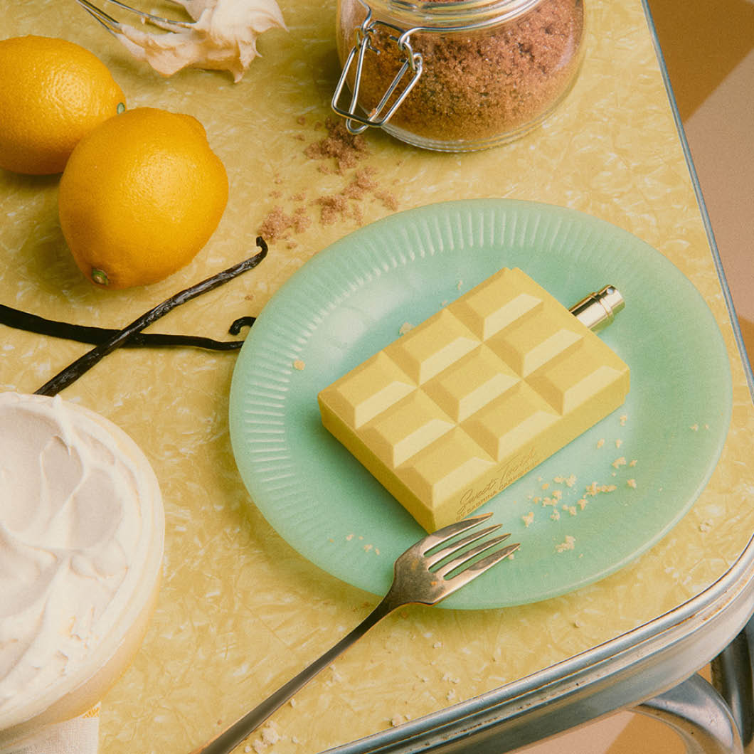 Markkinointikuva Sabrina Carpenter -tuoksusta. Pullo on asetettu lautaselle leivonnaisten ja sitruunoiden viereen, teksti ”Only at KICKS!”.