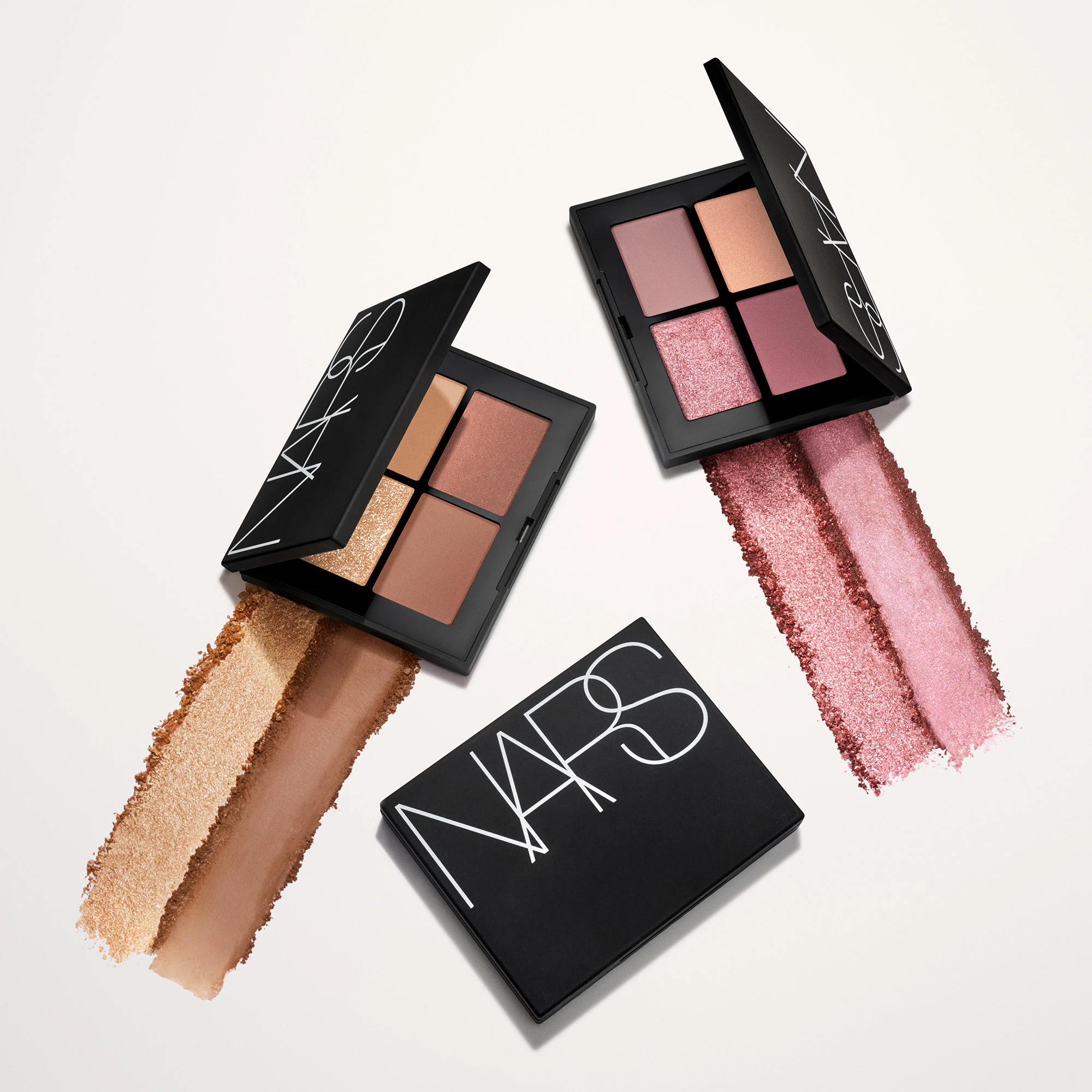Tre NARS øyenskyggepaletter vises mot en lys bakgrunn, hvorav to er åpne med fire nyanser hver i beige, brune, rosa og skimrende toner. Synlig tekst: “NARS” på lokkene, og utstrøkne øyenskygger viser pigmenter i gull-, brun-, rosa- og roséglitrende nyanser.