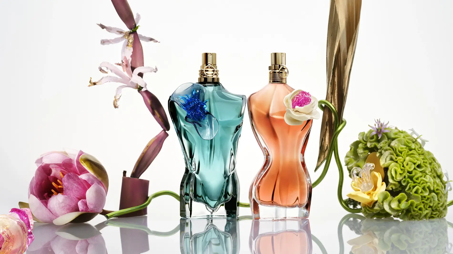 Jean Paul Gaultier, La Belle och Le Beau Flower Edition. Kaksi vartalon muotoista hajuvesipulloa värikkäiden kukkien ympäröimänä kiiltävällä pinnalla.