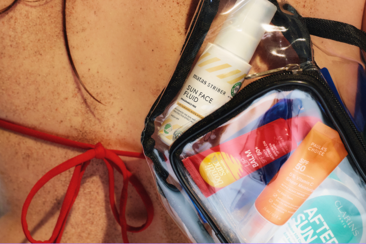 Närbild på en person i röd bikini med en genomskinlig necessär som innehåller solskydd och hudvård, inklusive Matas Striber Sun Face Fluid, Bondi Sands Lip Balm SPF 50+, Paula’s Choice SPF 50 5% Vitamin C Sheer Moisturizer och Clarins After Sun.