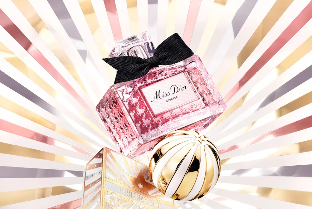 Miss Dior damparfym med guldflaska på strålande vit och roséguld bakgrund samt julkula i guld/vitt.