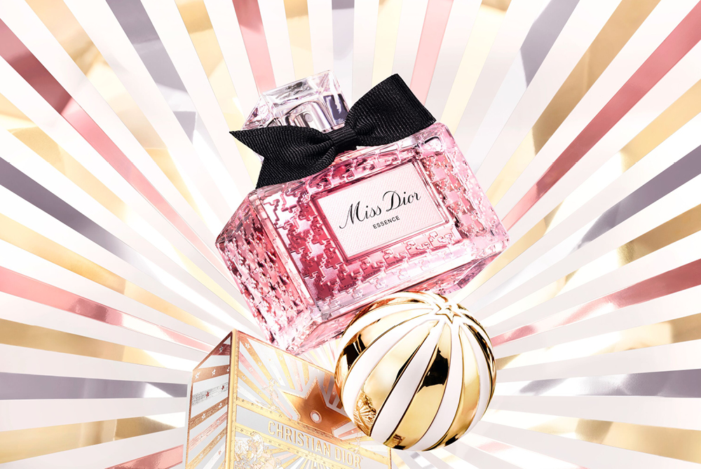 Miss Dior dameparfyme i gullflaske mot strålende hvit og roségull bakgrunn med gullkule.