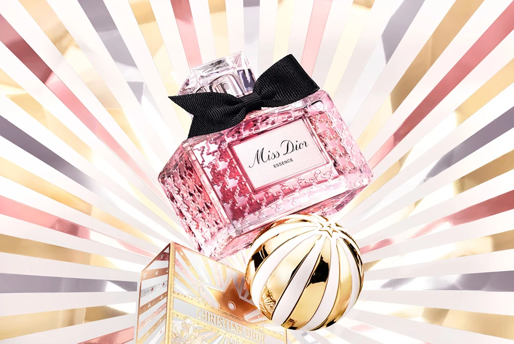 Miss Dior naisten hajuvesi kultaisessa pullossa, valkoinen ja ruusukultainen tausta, kultainen joulupallo.