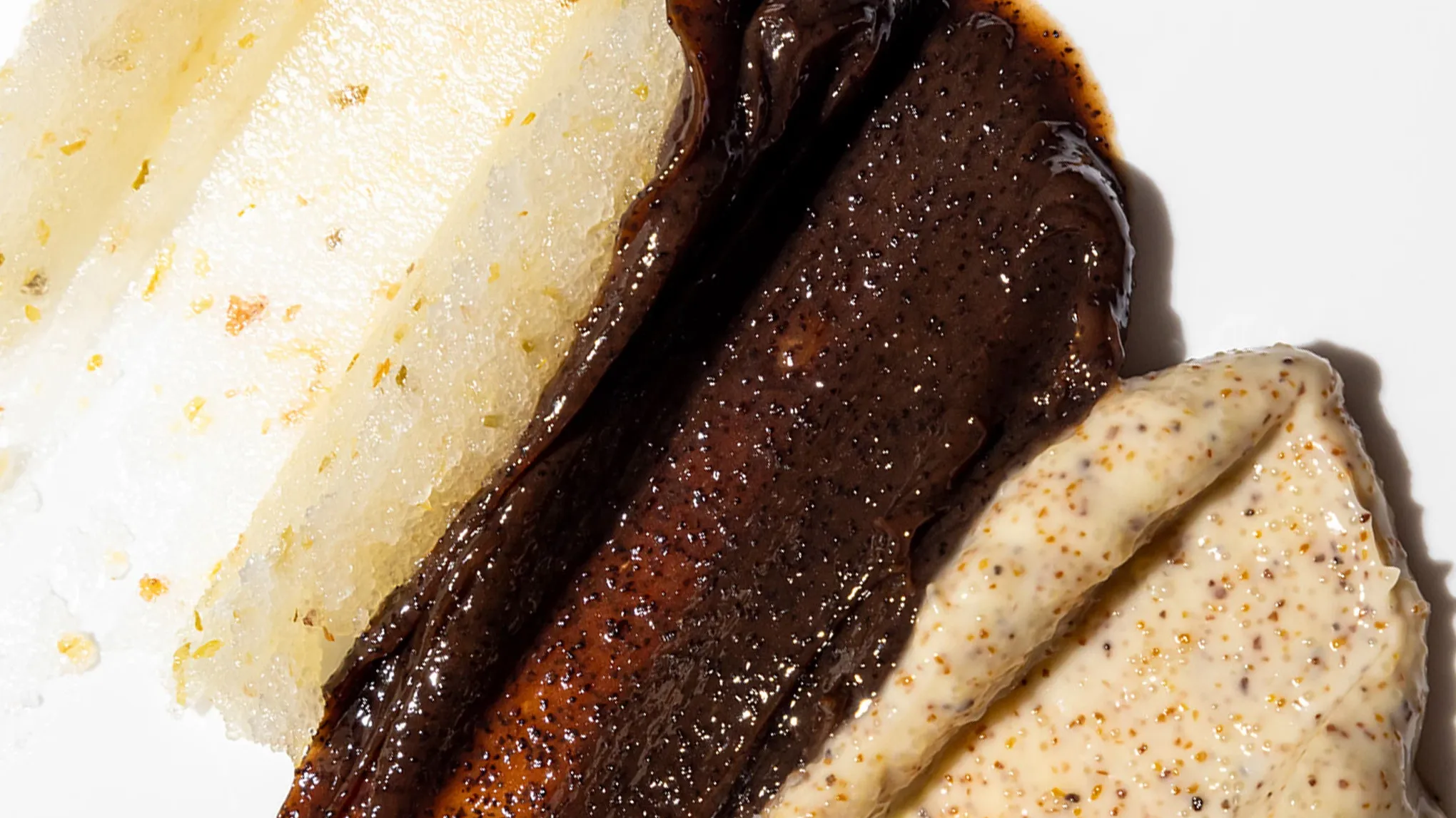 Närbild av tre olika ansiktsskrubbar i varierande färger och texturer på vit bakgrund