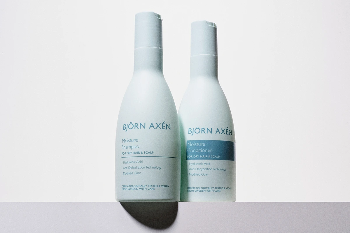 Björn Axén Moisture Shampoo ja Moisture Conditioner. Molemmat tuotteet ovat vaaleansinisissä pulloissa. Pullot seisovat vierekkäin valkoista taustaa vasten.