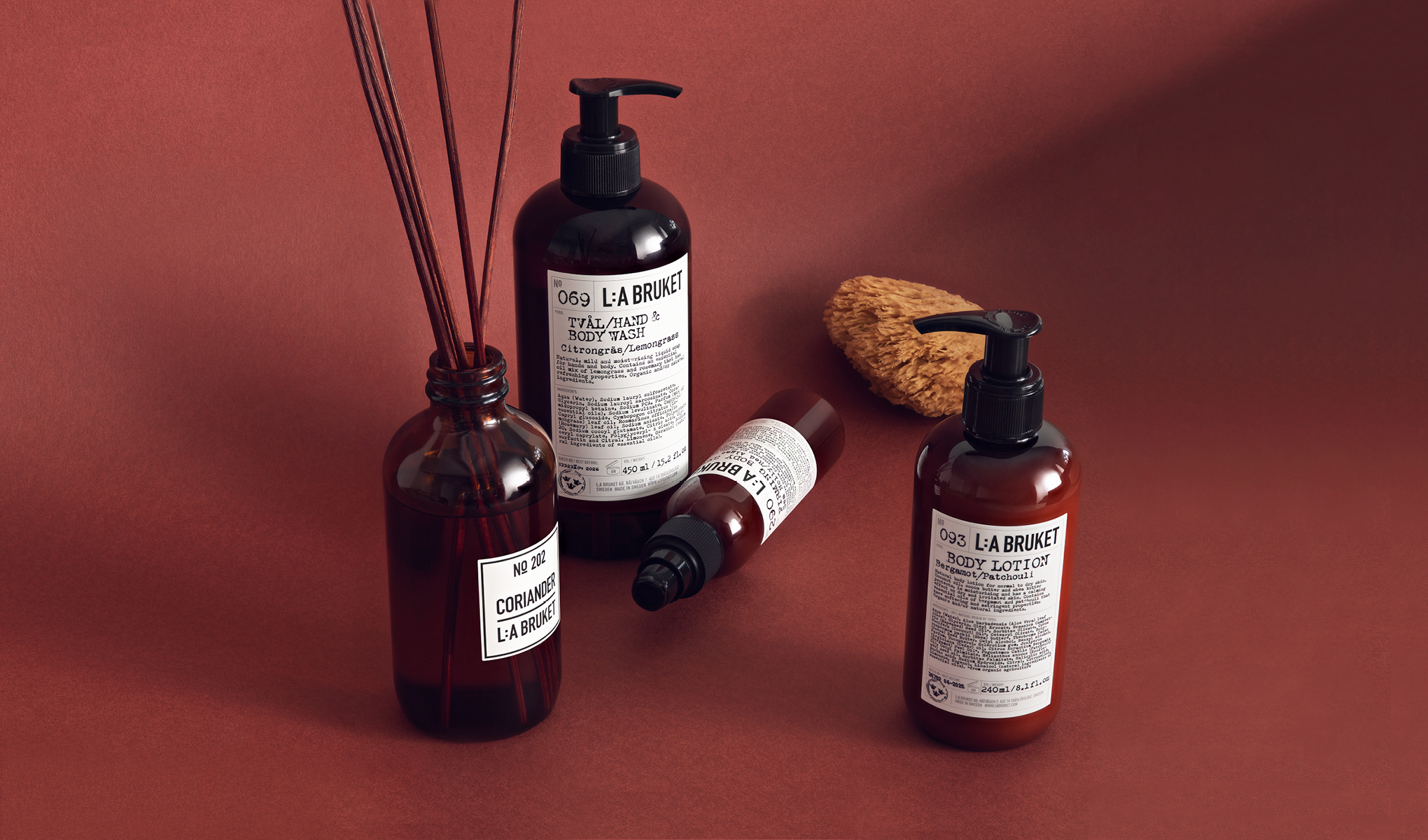 En kolleksjon med hudpleieprodukter fra L:A Bruket. Produktene er plassert på en rødbrun bakgrunn sammen med en natursvamp.