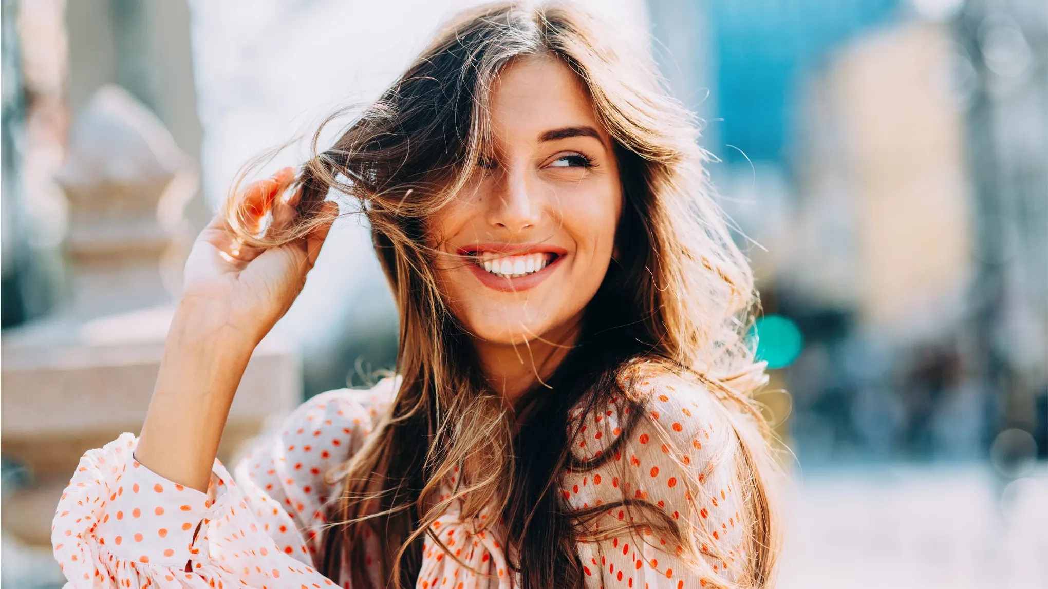 Hymyilevä tyttö, jolla on ruskeat hiukset pitelee hiussuortuvaa.