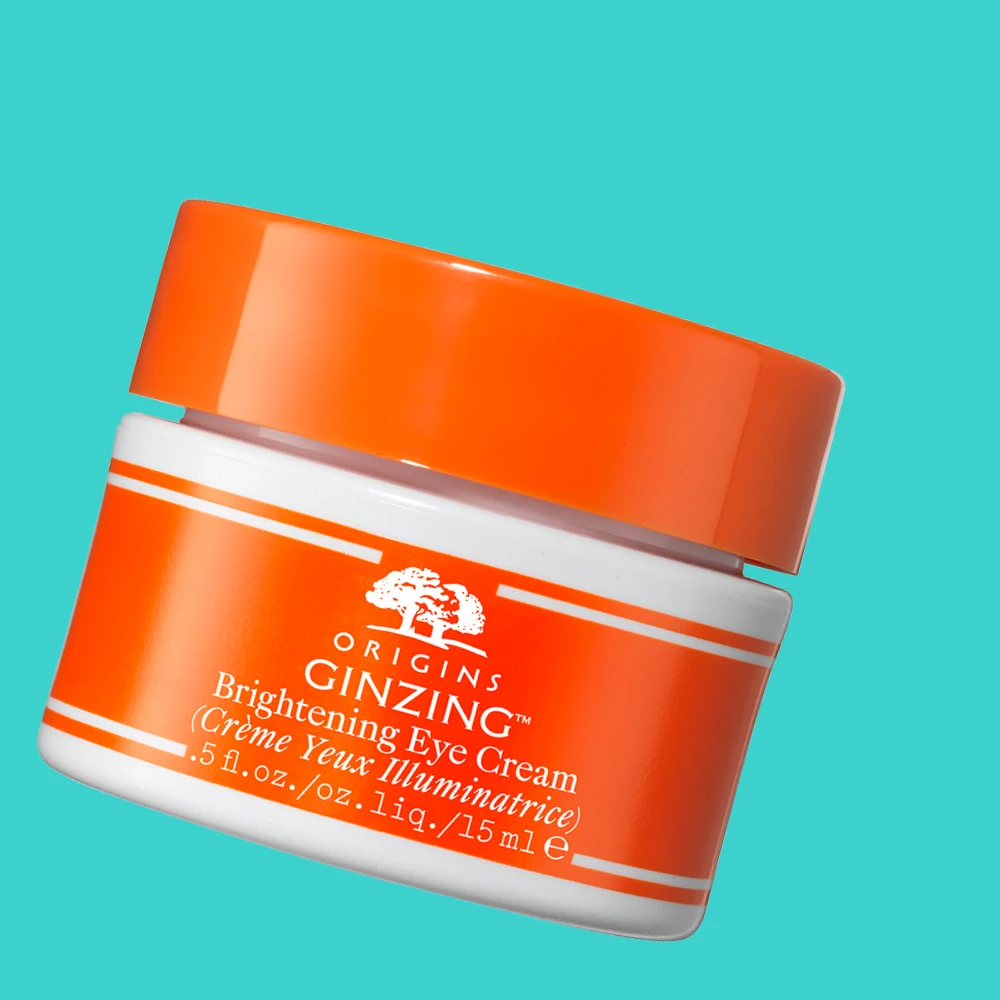 Origins GinZing Brightening Eye Cream -silmänympärysvoide. Oranssi ja valkoinen purkki turkoosilla taustalla.