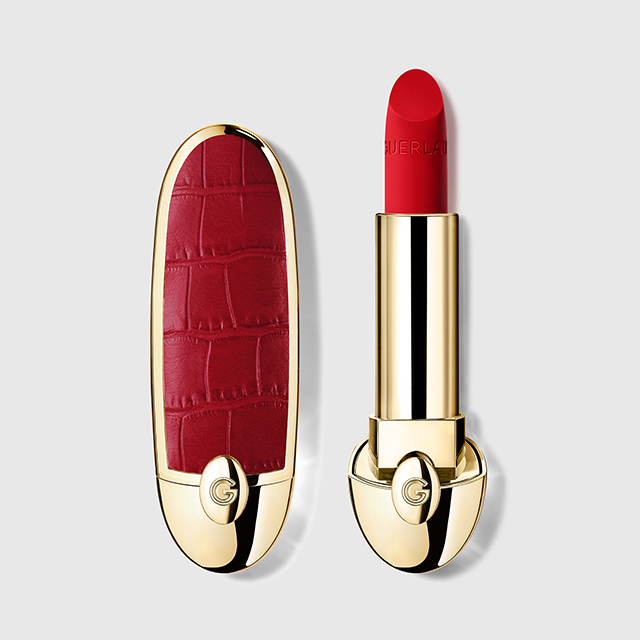 Rött läppstift från Guerlain med guldfärgad hylsa och röd, mönstrad kork med logotypen “G”. Läppstiftet är uppskruvat och visar en intensiv röd nyans med texten “GUERLAIN” präglad på produkten.