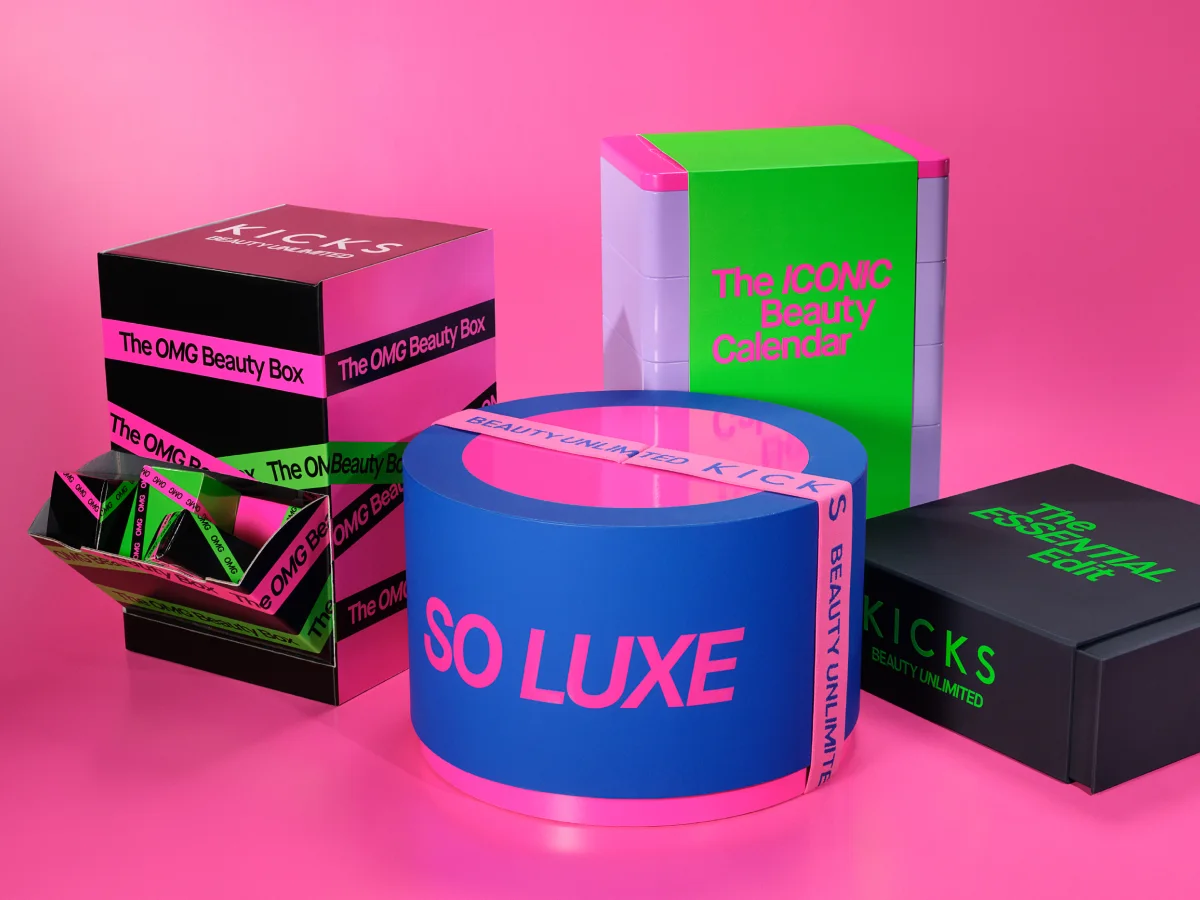 Fargerike KICKS-gaveesker mot rosa bakgrunn med tekstene “KICKS BEAUTY UNLIMITED”, “The OMG Beauty Box”, “The ICONIC Beauty Calendar”, “SO LUXE” og “The ESSENTIAL Edit”.