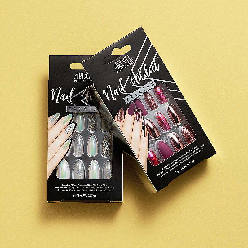 Pakkaukset Ardell Professional Nail Addict Premium irtokynsiä. Toinen pakkaus sisältää hologrammi- ja hopeanvärisiä kynsiä ja toinen pakkaus sisältää kynsiä vaaleanpunaisissa, violeteissa ja kimaltelevissa väreissä. Pakkaukset on sijoitettu keltaiselle taustalle.