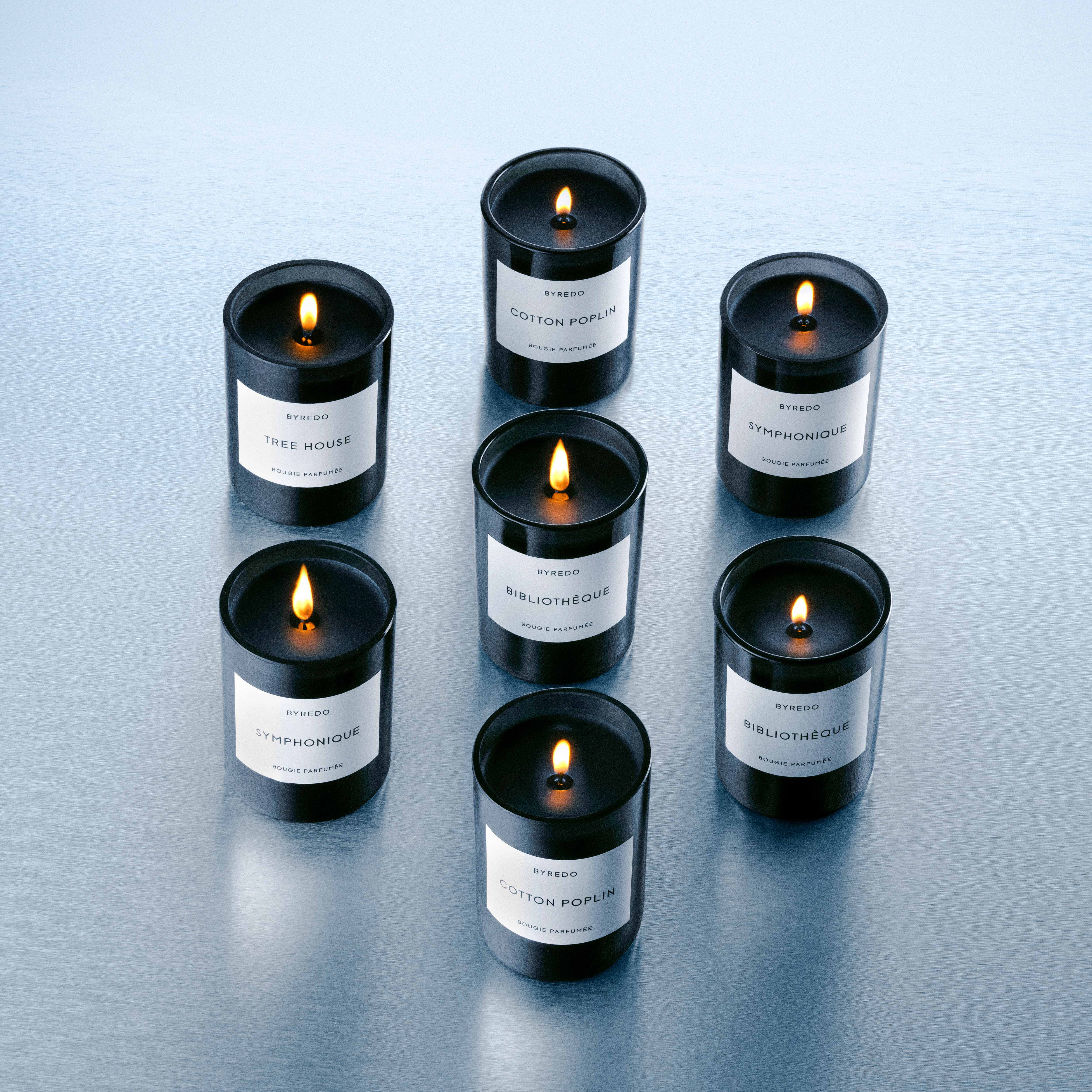 Useita Byredo-tuoksukynttilöitä palamassa riveissä vaalealla pinnalla.