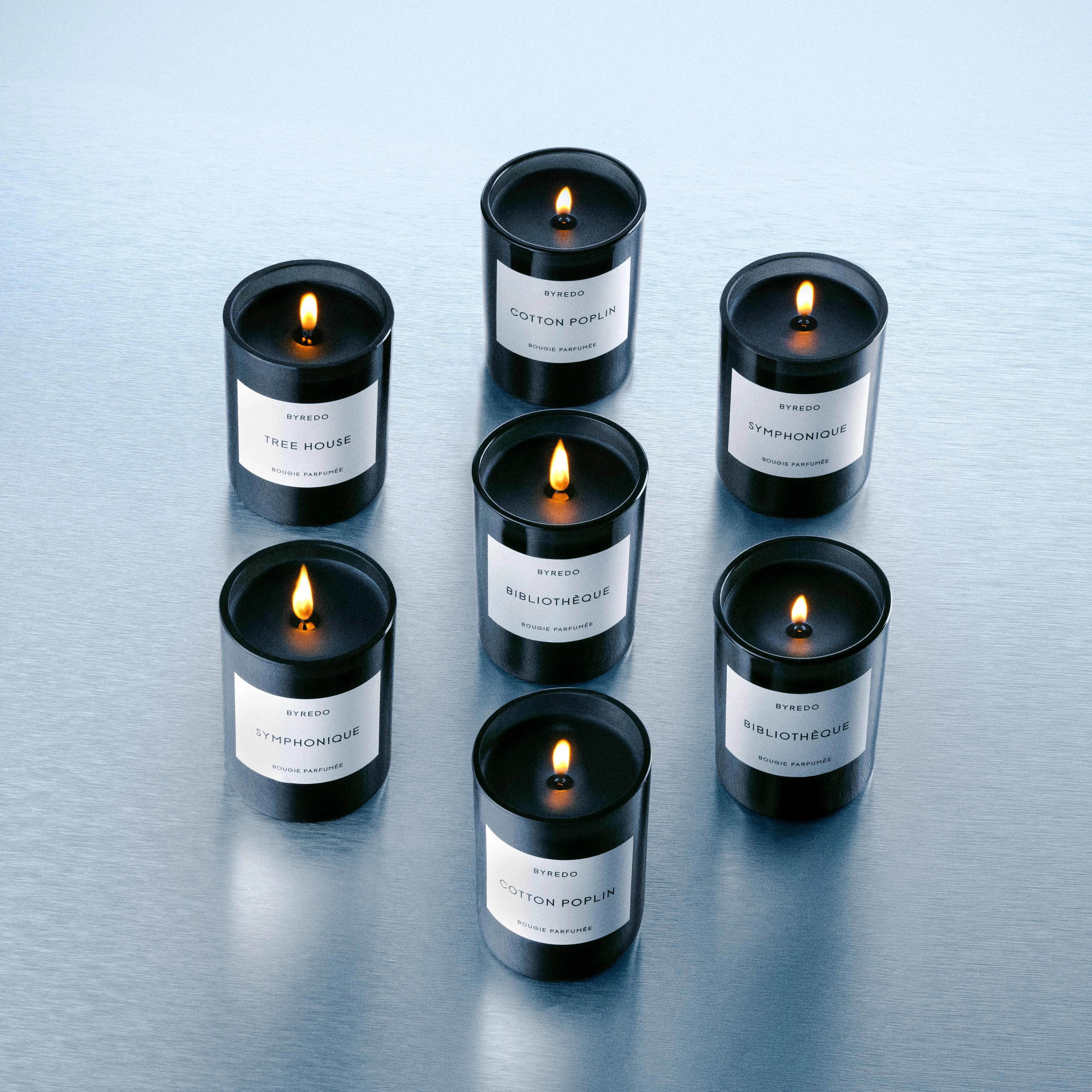 Flera Byredo doftljus tända i rader på ljus yta.