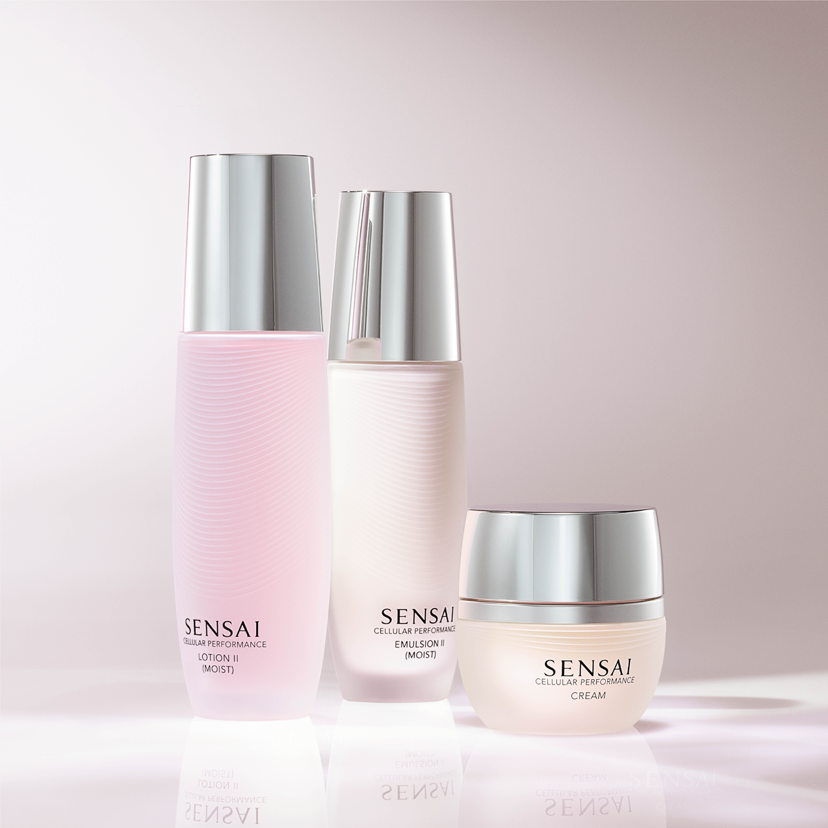 Kolme SENSAI Cellular Performance -ihonhoitotuotetta vaaleanpunaisella taustalla: Lotion II (Moist), Emulsion II (Moist) ja Cream. Tuotteissa on pehmeät vaaleanpunaiset ja valkoiset sävyt sekä hopeanväriset korkit, jotka luovat ylellisen vaikutelman kosteuttavasta skincare- ja kasvovoidevalikoimasta.