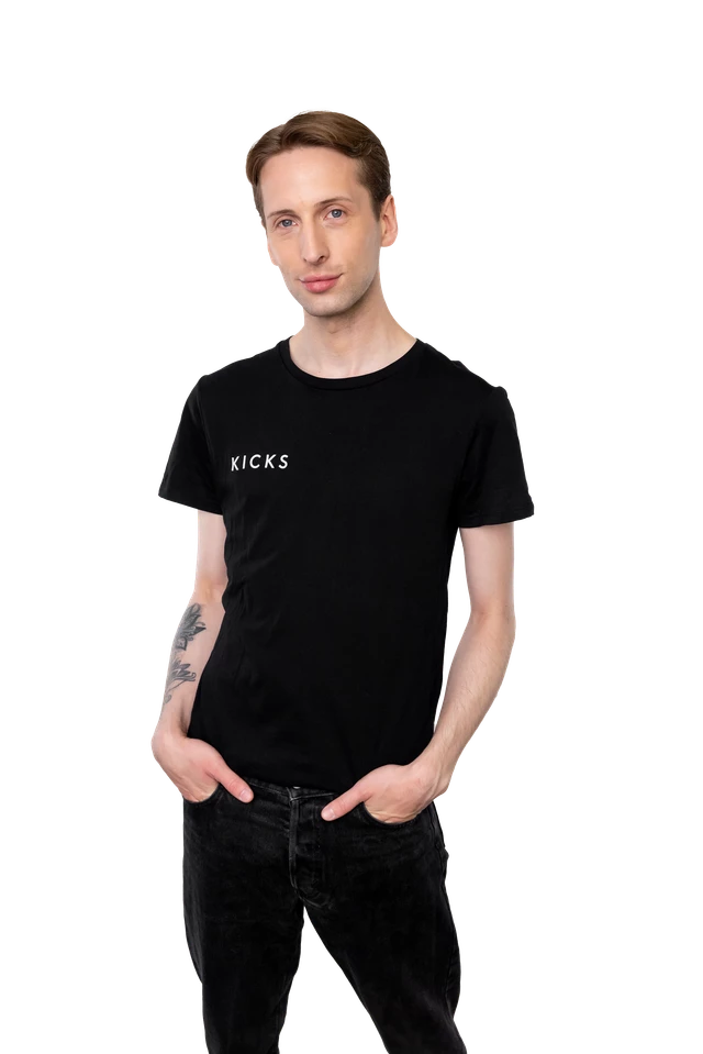 Henkilö, jolla on musta KICKS-paita ja mustat farkut, kädet taskuissa.