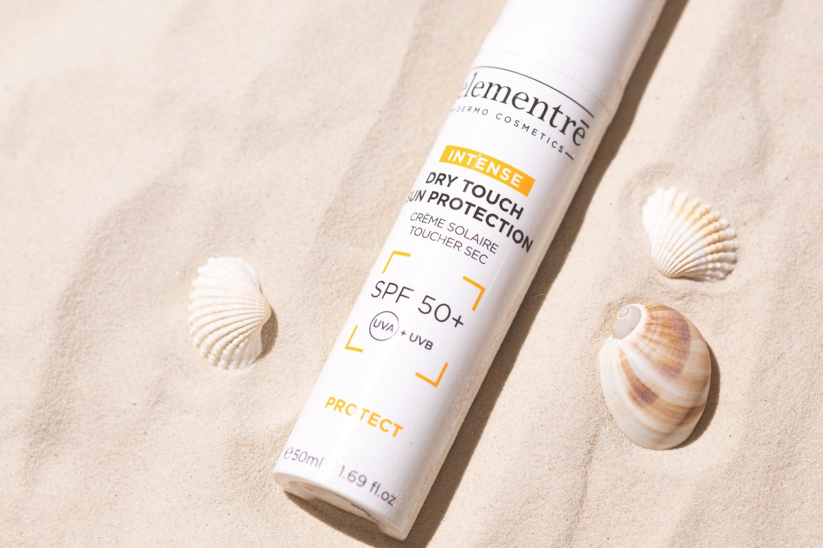 Pullo intensiivistä aurinkovoidetta SPF 50+ hiekalla, ympärillä kauniita simpukoita. 