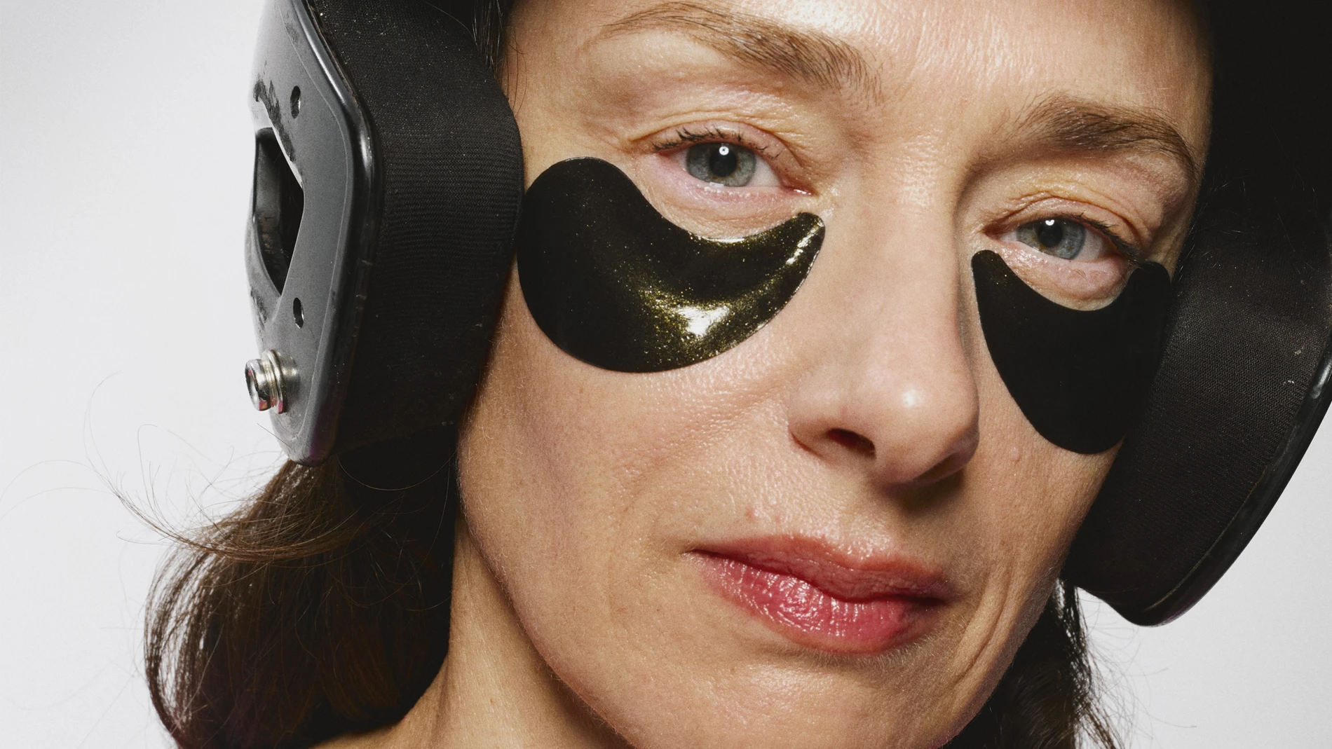 Person med langt mørkt hår og rosa genser som har på seg en svart hjelm og svarte eye patches under øynene