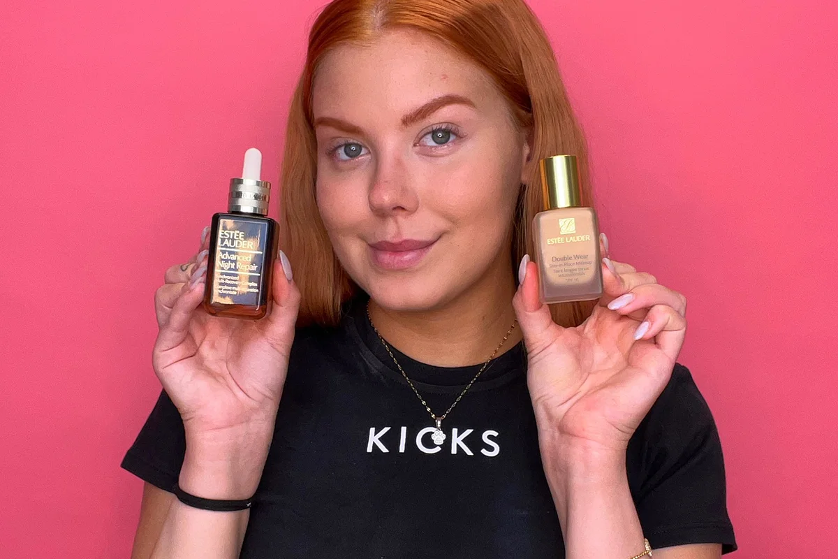 KICKS medarbetare håller upp två Estée Lauder-produkter – ett serum med pipett i vänster hand och en foundationflaska i höger hand