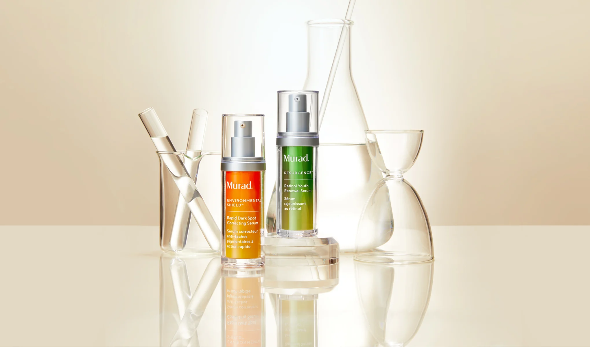 Två serumflaskor från Murad placerade på en reflekterande yta. Den vänstra flaskan är orange och märkt "Environmental Shield Rapid Dark Spot Correcting Serum", medan den högra flaskan är grön och märkt "Resurgence Retinol Youth Renewal Serum". Bakgrunden består av olika laboratorieglas, inklusive provrör och bägare, vilket ger en vetenskaplig känsla.