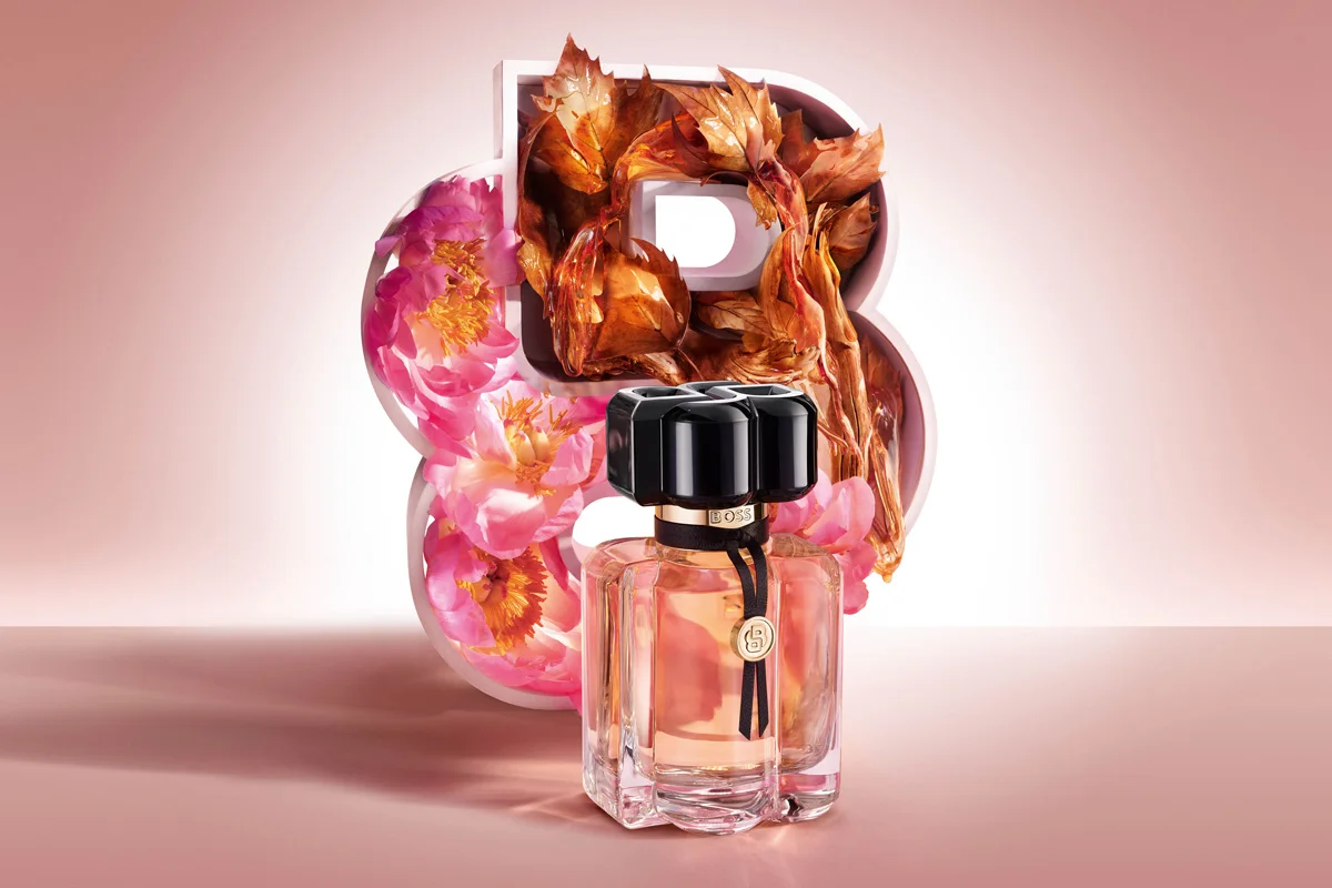 Boss The Scent-parfym mot rosa bakgrund framför blommor och höstlöv.