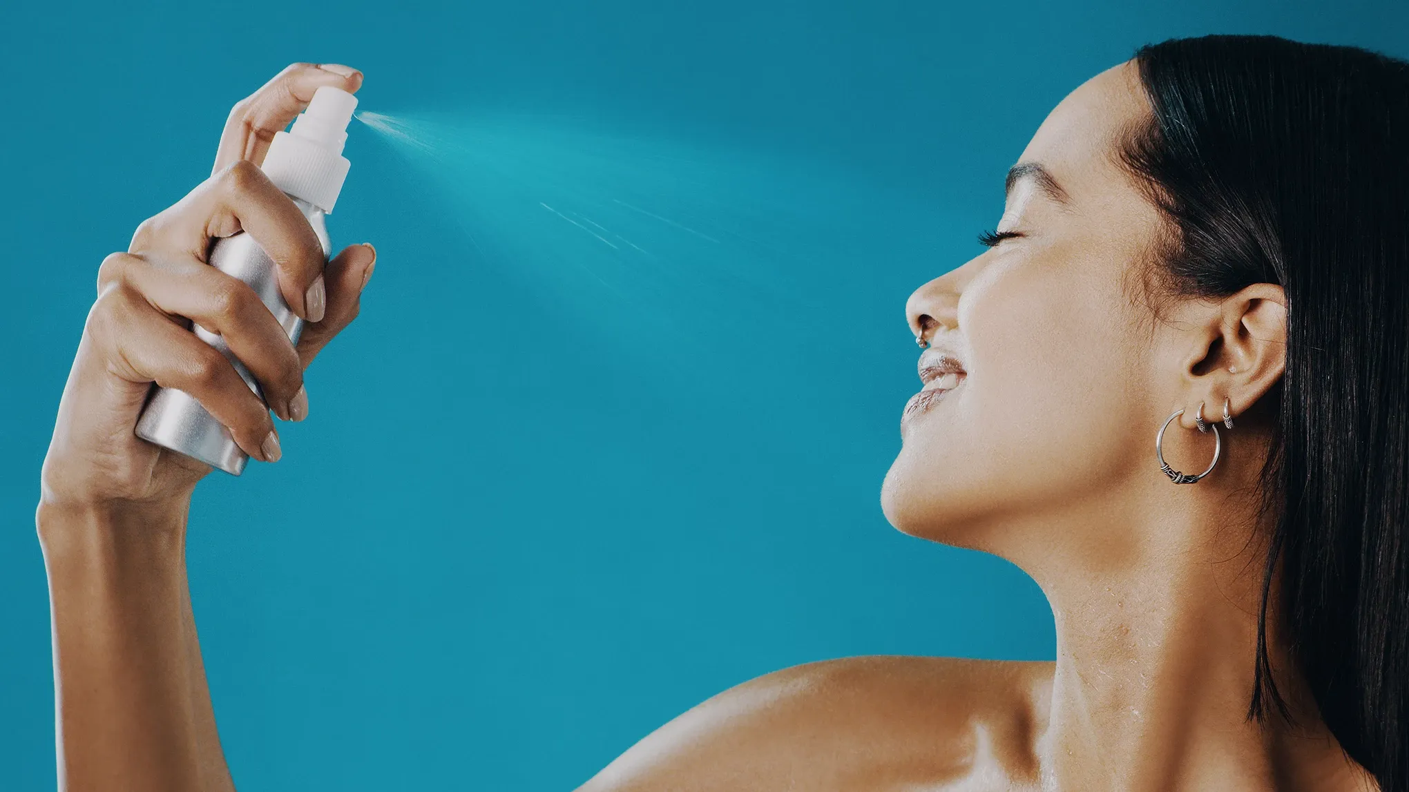 Kvinna som sprayar SPF-mist mot sitt ansikte mot en blå bakgrund.