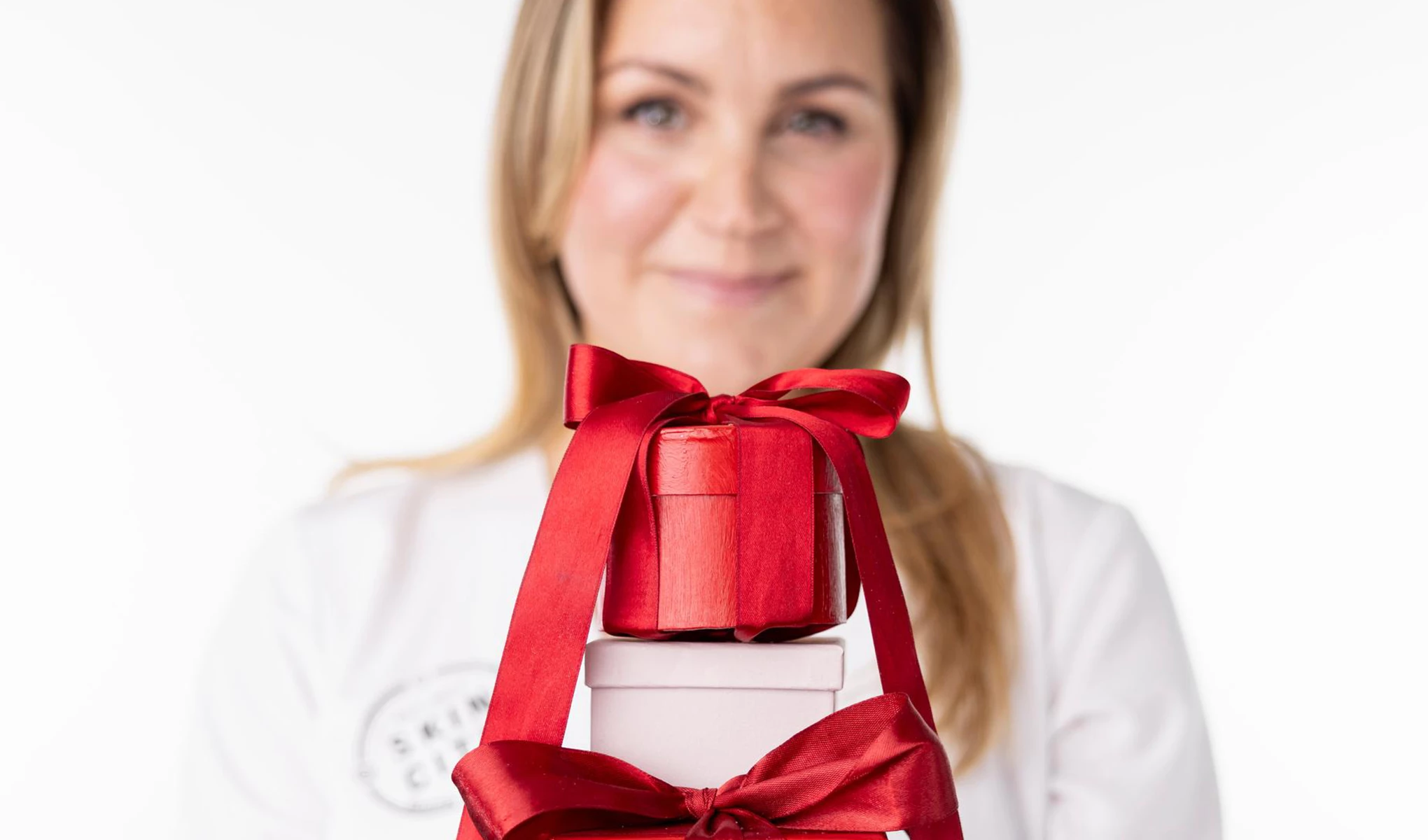 Små presentaskar i rött och rosa, prydda med röda rosetter, med en suddig kvinna i bakgrunden.