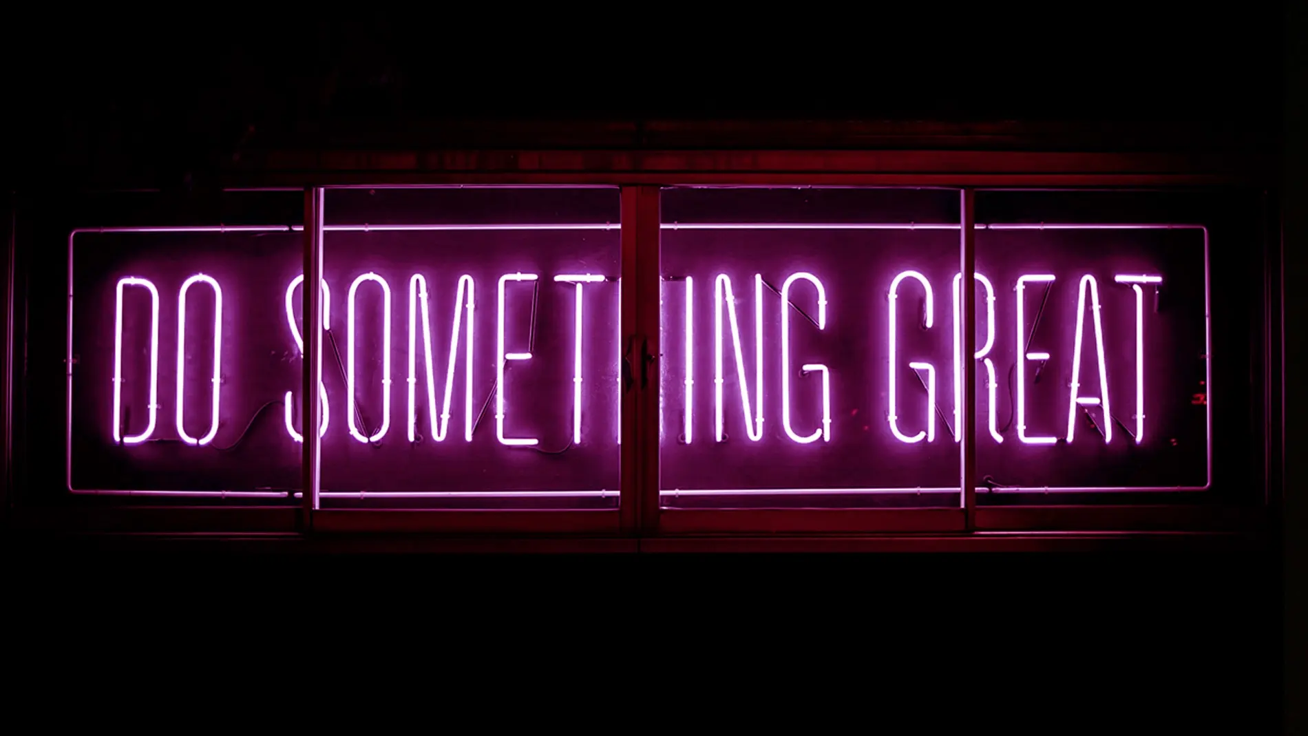 Rosa neonskilt med teksten "Gjør noe flott" mot en mørk bakgrunn.