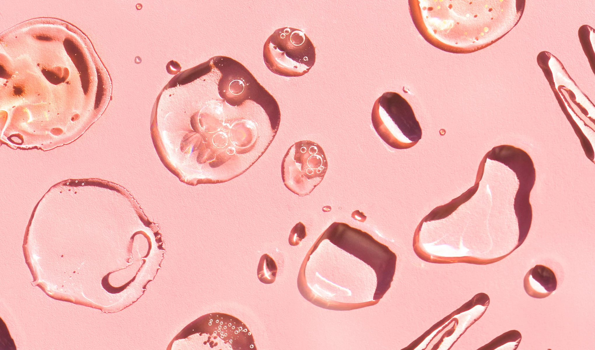 Närbild av genomskinliga droppar på en rosa yta.
