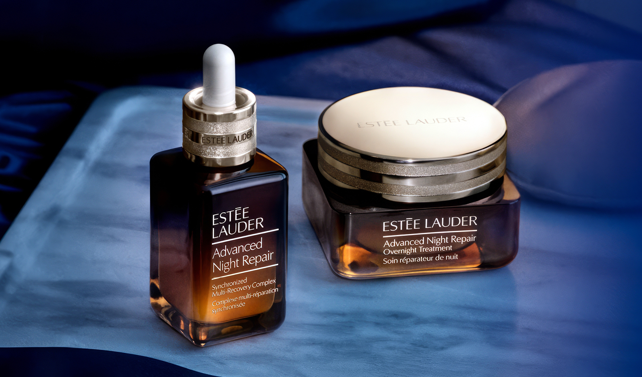 To hudpleieprodukter fra Estée Lauder plassert på en blå silkebakgrunn.