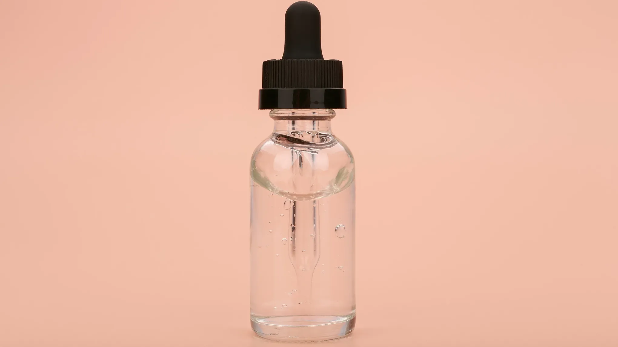 Gjennomsiktig pipetteflaske med hudpleieserum mot beige bakgrunn