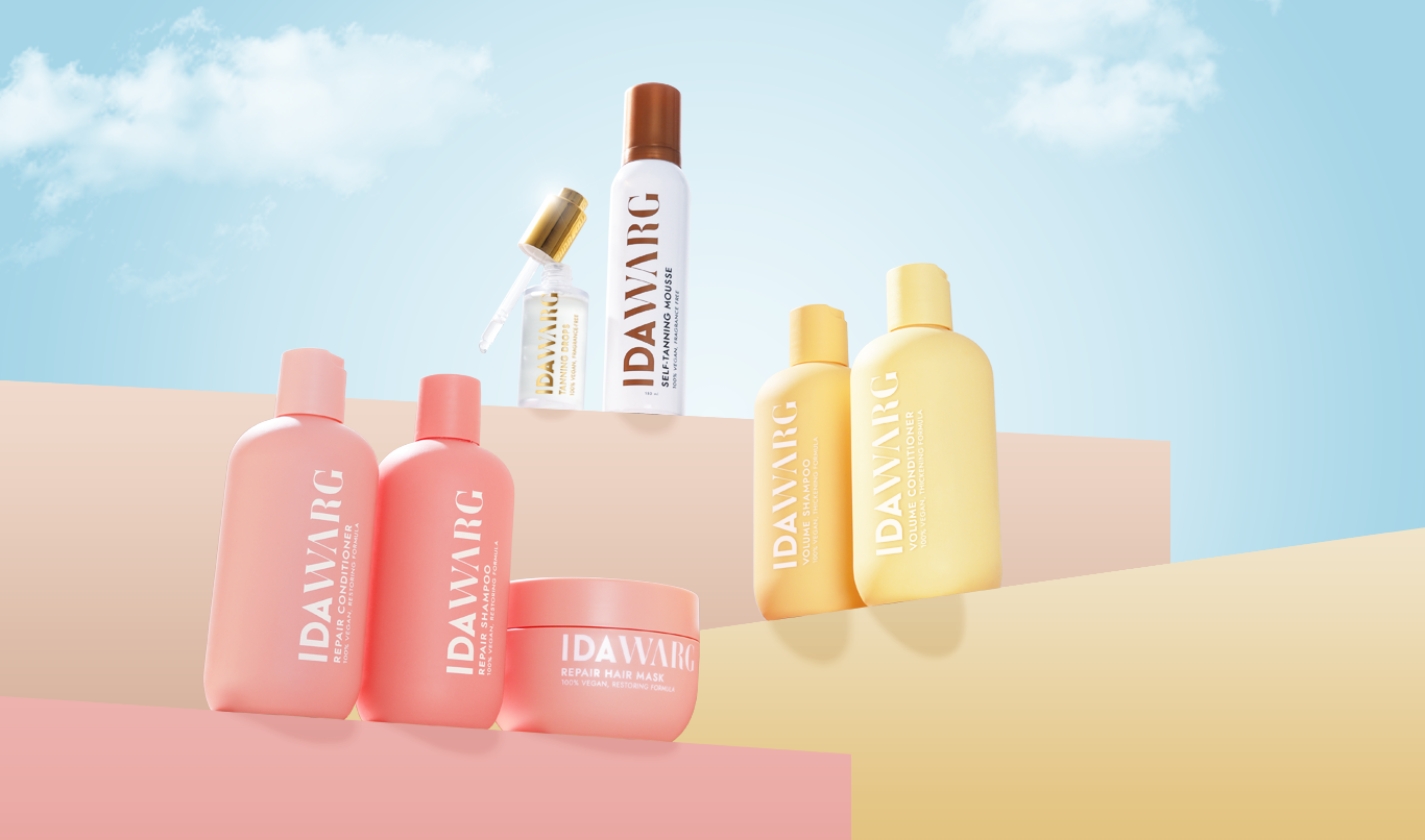 Flere hårpleieprodukter fra Ida Warg. Produktene er arrangert på en fargerik flate med himmel og skyer i bakgrunnen. Flaskene er i rosa og gule nyanser.