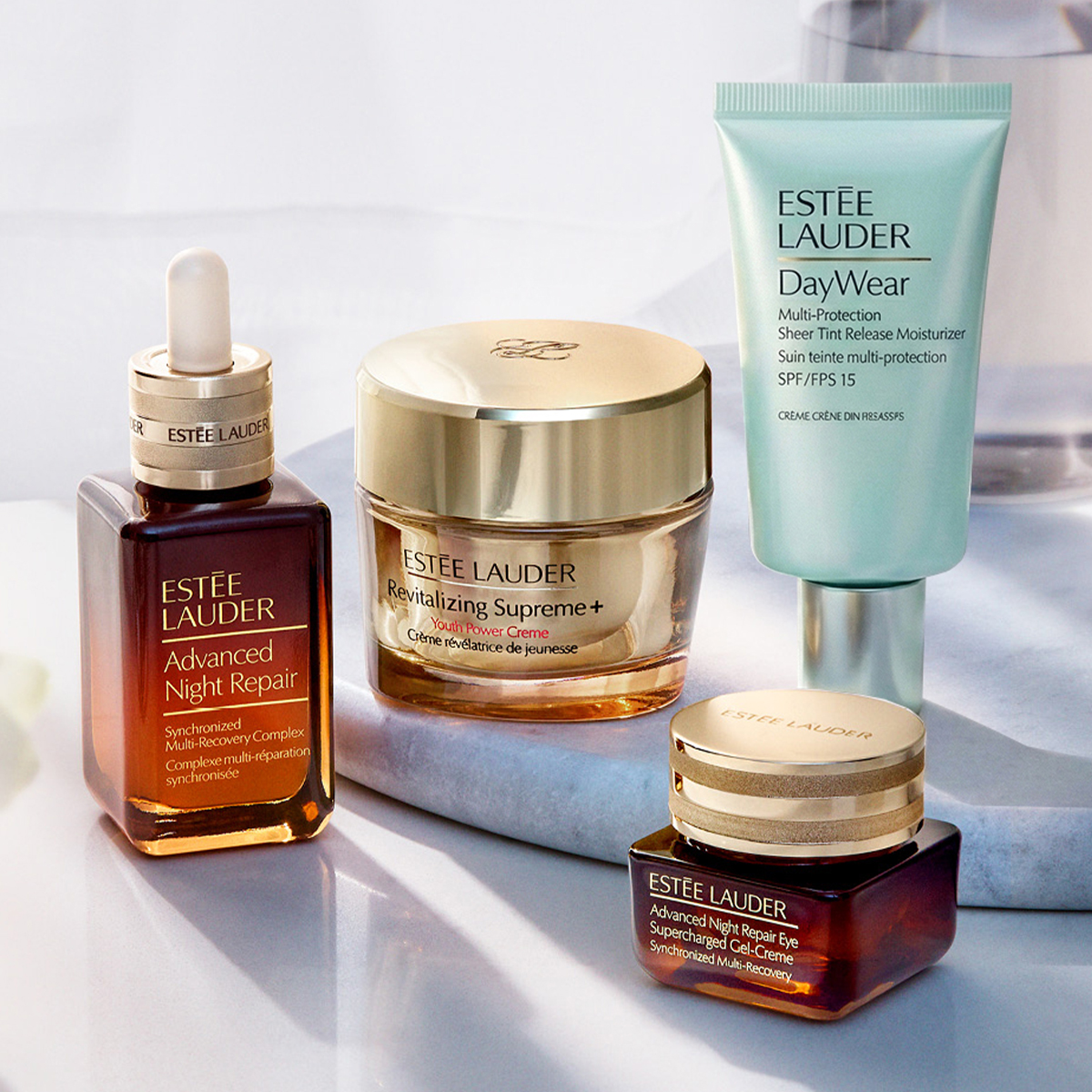 Tre hudpleieprodukter fra Estée Lauder plassert på en marmorflate mot en lys bakgrunn.