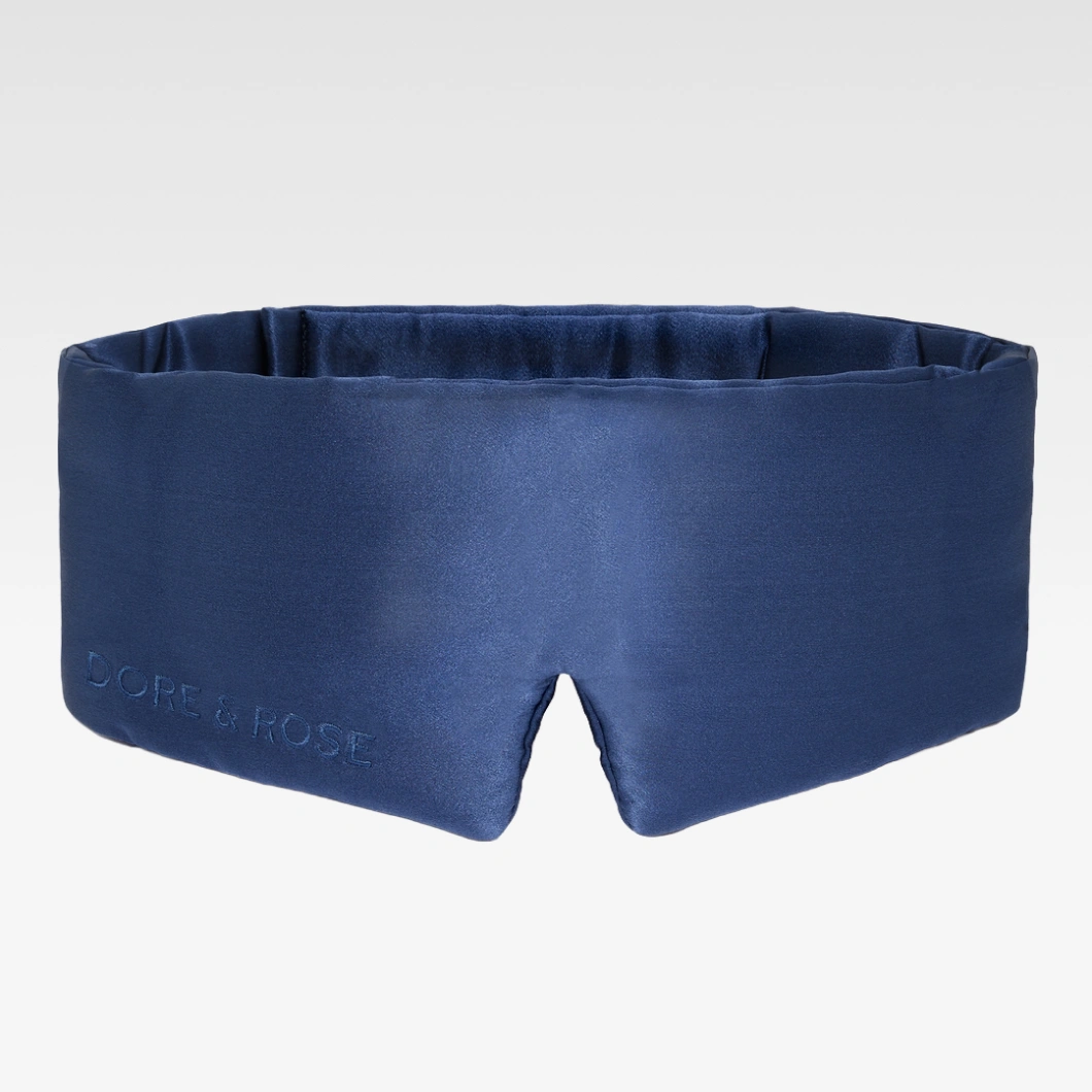 Mörkblå sovmask i satin från DORE & ROSE på ljusgrå bakgrund. Mjuk och vadderad design för sömn och avslappning.