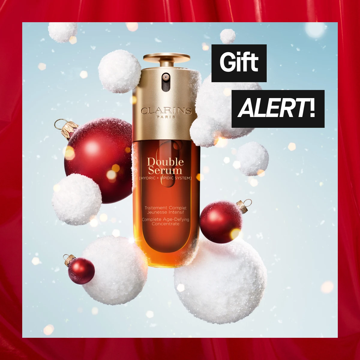 Clarins Double Serum med gyllene lock svävar bland vita snöbollar och röda julkulor mot ljusblå bakgrund – ikonisk anti-age hudvård i vintrig julkampanj.