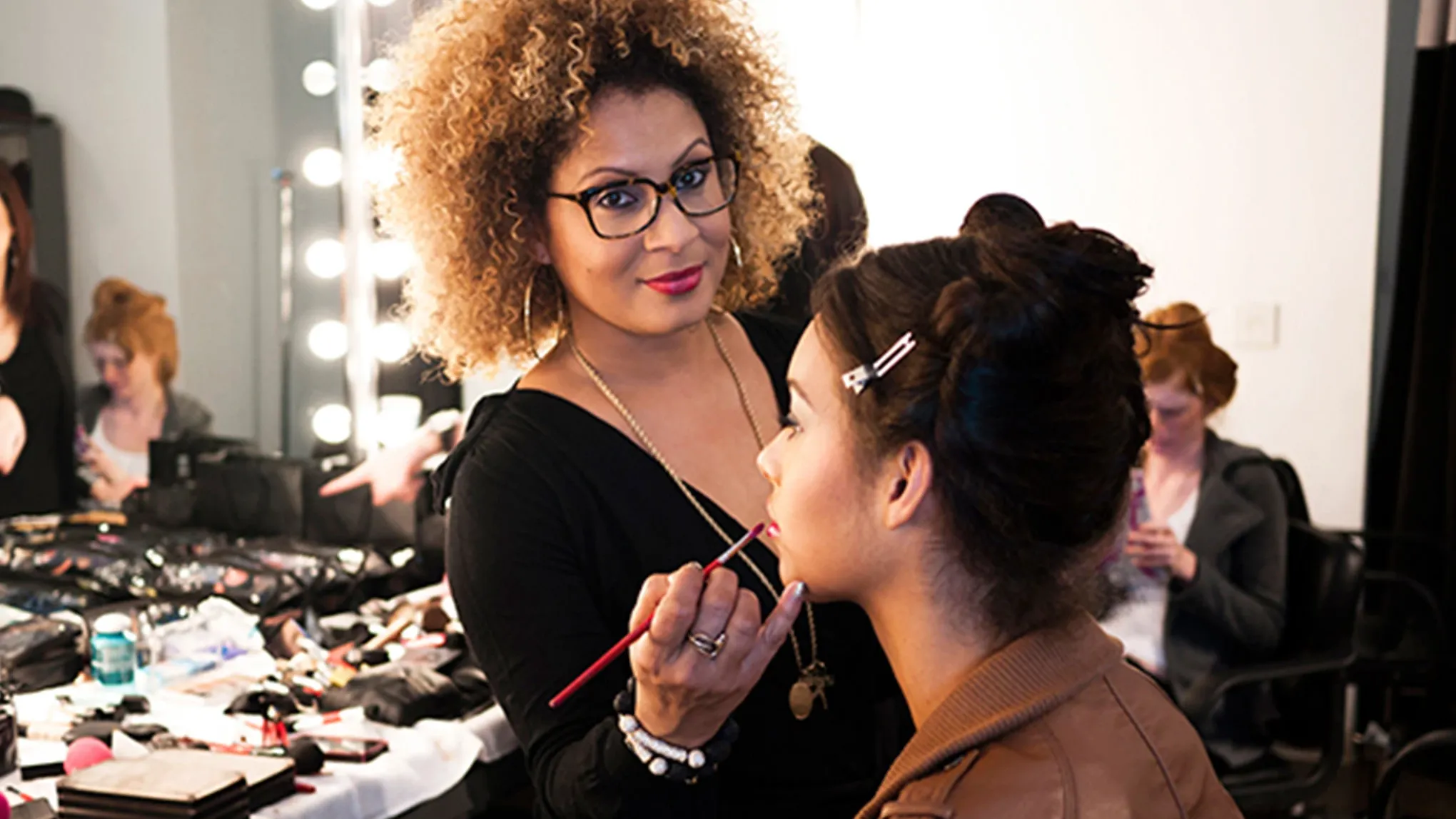 Makeupartist påfører leppefarge på en kvinne i sminkestudio.