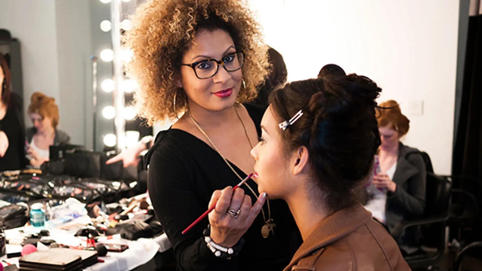 Makeupartist påfører leppefarge på en kvinne i sminkestudio.