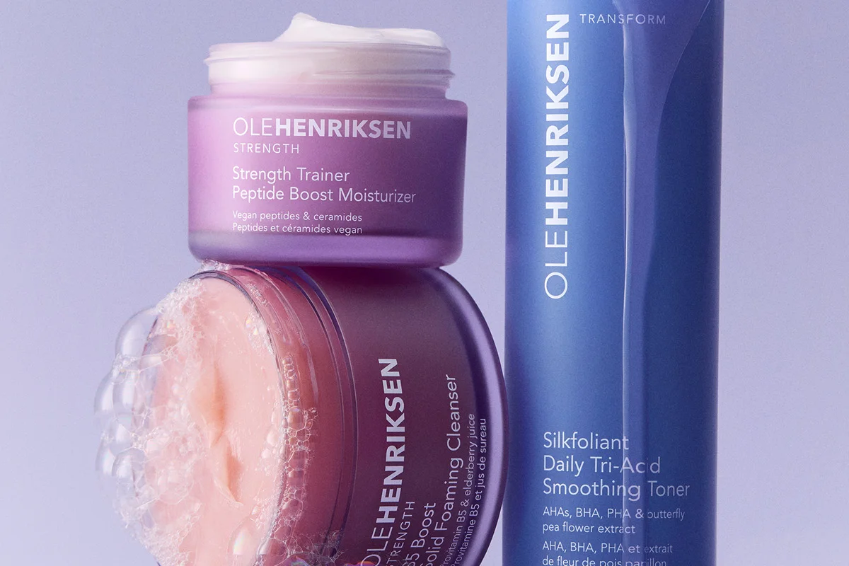 OLEHENRIKSEN hudvård med Strength Trainer Peptide Boost Moisturizer, Truth Juice Daily Cleanser och Transform Silkfoliant Daily Tri-Acid Smoothing Toner. Produkterna visas i lila och blå förpackningar med synlig text som “Vegan peptides & ceramides”, “AHAs, BHA, PHA & butterfly pea flower extract” samt skumdetaljer runt rengöringen.