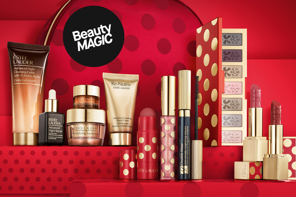 Estée Lauder sminke- og hudpleiesett i flere deler mot rød julebakgrunn/gaveesker med "Beauty MAGIC"-klistremerke på rød prikkete bakgrunn.