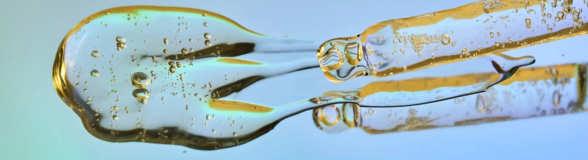 Pipett med serum på en spegelblank blå turkos yta. 