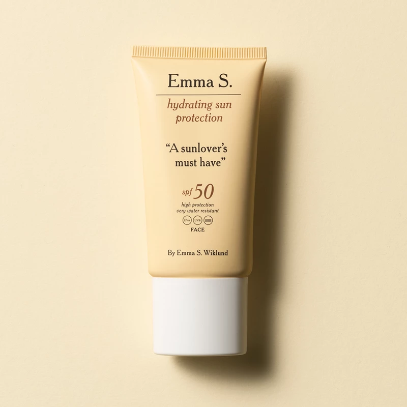 Keltainen tuubi Emma S:n kosteuttavaa aurinkosuojavoidetta SPF 50, jonka etupuolella on teksti ”A sunlover's must have” kirkkaan keltaisella pohjalla.